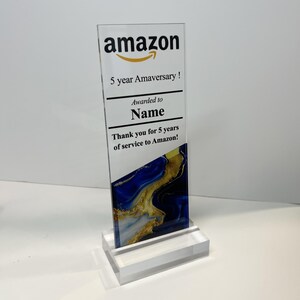 Puede incluir: Una placa de premio de acr&iacute;lico transparente con un dise&ntilde;o de m&aacute;rmol azul y dorado. La placa tiene el logotipo de Amazon y el texto "5 year Amaversary! Awarded to Name Thank you for 5 years of service to Amazon!"
