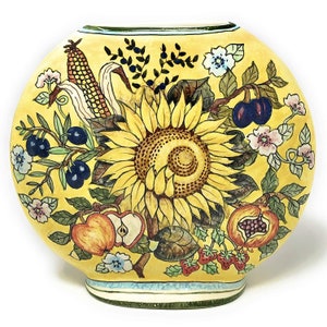 May include: A yellow ceramic vase with a floral design featuring a sunflower, corn, apples, berries, and pomegranates. The vase has a rounded shape and a green and blue rim.