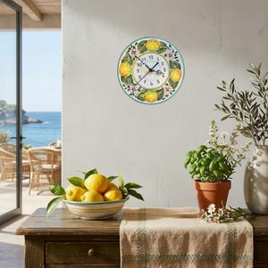 May include: A round wall clock with a lemon design. The clock face is white with black numbers and hands. Lemons and flowers decorate the border. The clock is mounted on a white wall.