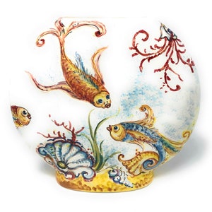 May include: A white ceramic vase with hand-painted aquatic scene. The design features orange, blue, and yellow fish swimming among coral and seaweed. The vase has a rounded shape with a yellow base.