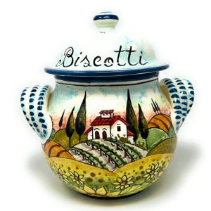 May include: A ceramic cookie jar with a blue and white lid and a painted scene of a house in a Tuscan landscape. The lid has the word "Biscotti" written on it.