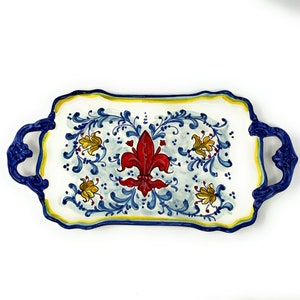 May include: A white ceramic serving tray with blue and yellow floral designs and a red fleur-de-lis in the center. The tray has two blue handles.