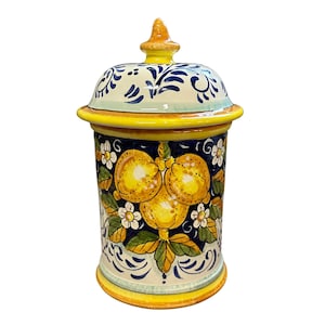 May include: A ceramic jar with a lid, featuring a hand-painted design. The jar is cylindrical with a yellow base and rim, and a blue and white floral pattern. The main design showcases yellow lemons and white flowers.