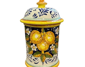 May include: A ceramic jar with a lid, featuring a hand-painted design. The jar is cylindrical with a yellow base and rim, and a blue and white floral pattern. The main design showcases yellow lemons and white flowers.