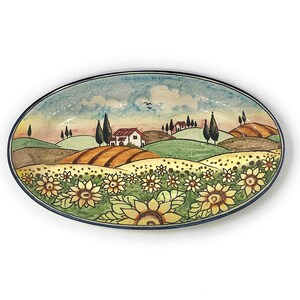 Könnte beinhalten: Eine ovale Servierplatte aus Keramik mit handbemaltem Motiv einer toskanischen Landschaft. Die Platte zeigt sanfte Hügel, ein kleines Haus, Zypressen und ein Sonnenblumenfeld.