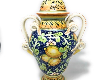 May include: A ceramic vase with a lid, featuring a blue and yellow floral design with lemons. The vase has two handles and a round base.