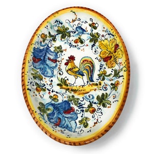 May include: An oval ceramic platter featuring a central hand-painted rooster in yellow, blue, and red. The border is a warm yellow with brown accents, and the surrounding design includes blue and yellow floral motifs and green foliage.