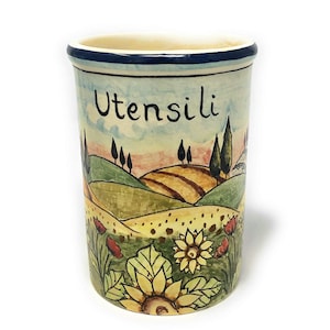 Op de afbeelding: Een keramische bestekhouder met een handgeschilderd ontwerp van een Toscaans landschap. De houder is versierd met zonnebloemen, bomen en glooiende heuvels. Het woord "Utensili" staat op de voorkant van de houder.