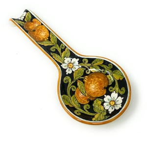 May include: A ceramic spoon rest with a black background and a floral design featuring orange fruit and white flowers. The spoon rest has a brown rim.
