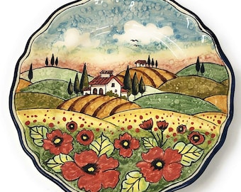 May include: A ceramic plate with a hand-painted design of a Tuscan landscape. The scene features rolling hills, a small white house, and red poppies in the foreground. The plate has a blue and white border.