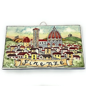 Puede incluir: Un azulejo de cerámica colorido que representa una vista de la ciudad de Florencia, Italia. El azulejo presenta una ilustración detallada del Duomo, la catedral icónica de la ciudad, con su cúpula distintiva y los edificios circundantes. El azulejo está pintado en una paleta vibrante de rojos, amarillos, verdes y azules, con una pancarta en la parte inferior que dice "Firenze".