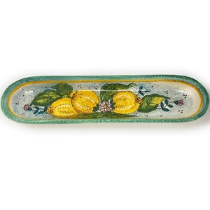 May include: A long, oval ceramic serving dish with a green rim and a blue and white background. The dish is decorated with three yellow lemons and green leaves.