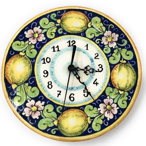 May include: A blue and yellow ceramic clock with a lemon design. The clock face has Roman numerals and a black hour and minute hand.