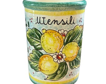 Può includere: Un portautensili in ceramica con un disegno dipinto a mano di limoni e foglie. Il portautensili cilindrico ha uno sfondo azzurro e la scritta "Utensili" in nero. Il bordo è verde.
