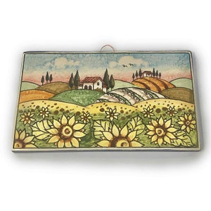May include: A hand-painted ceramic tile depicting a Tuscan landscape with rolling hills, a small house, and sunflowers in the foreground. The tile has a rustic, vintage aesthetic.