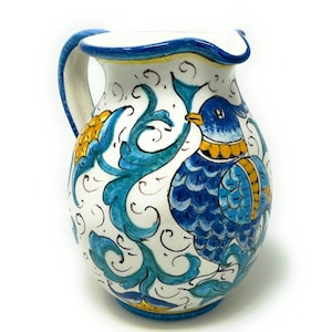 Könnte beinhalten: Eine weiße Keramikkanne mit einem blauen und gelben Blumendesign mit einem Vogel. Die Kanne hat einen Henkel und einen runden Körper.