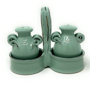 Op de afbeelding: Een zeegroene keramische zout- en peper set. De set bevat twee kleine potjes met handvatten, gemarkeerd met "Z" en "P", in een dubbelzijdige houder met een centrale handgreep. De set heeft een rustieke, verouderde uitstraling met bruine accenten.