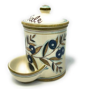 Peut inclure: Pot à sel en céramique crème avec couvercle et petit plat intégré. Le pot est décoré d'illustrations de branches d'oliviers et du mot "Sale" sur le couvercle. Le couvercle a un petit bouton avec des rayures vertes et bleues.