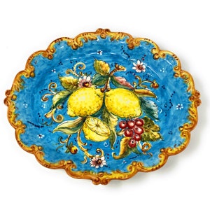 May include: A blue and gold ceramic platter with a hand-painted design of lemons, grapes, and flowers. The platter has a scalloped edge and a raised rim.