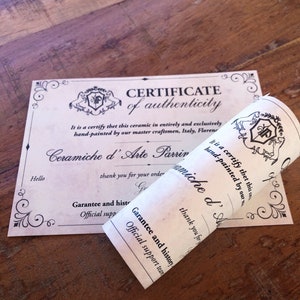 May include: A certificate of authenticity and a rolled-up paper with text. The certificate has decorative borders and the words "CERTIFICATE of authenticity". The rolled paper says "Ceramiche d'Arte Parrini" and "hand-painted".