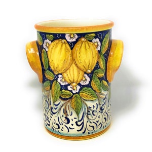 May include: Ceramic utensil holder with yellow lemons, green leaves, and white flowers on a blue background. The holder has two yellow handles.