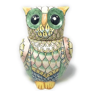 Könnte beinhalten: Eine Eulenfigur aus Keramik mit handbemaltem Design in den Farben Grün, Gelb, Rosa und Blau. Die Eule hat große grüne Augen, einen gelben Schnabel und detaillierte Federmuster auf dem Körper sowie gelbe Füße an der Unterseite.