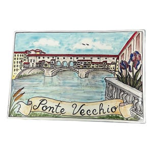 Peut inclure: Un carreau en céramique peint à la main représentant le Ponte Vecchio à Florence, en Italie. Le carreau présente un ciel bleu, une rivière et une bannière qui dit "Ponte Vecchio".
