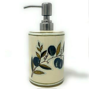 May include: Cream-colored ceramic soap dispenser with a stainless steel pump. The dispenser is decorated with a hand-painted olive branch design in shades of green, blue, and brown. The base and rim have a green border.