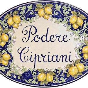 May include: Oval ceramic plaque with a cream-colored center and a blue border. The border features a repeating pattern of yellow lemons and green leaves. The words "Podere Cipriani" are written in elegant blue script.