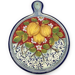 Puede incluir: Un plato de servir redondo de cerámica con un borde azul y un asa. El plato presenta un diseño pintado a mano de limones y hojas sobre un fondo rojo y blanco.