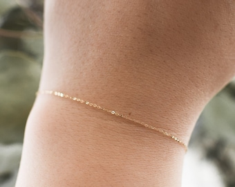 May include: A delicate gold chain bracelet on a person's wrist. The bracelet is thin and simple, with a subtle shine.