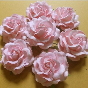May include: A bouquet of seven pink paper roses. The roses are arranged in a circle and have a slightly ruffled texture.