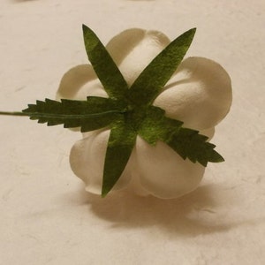 May include: A white paper flower with a green leaf design. The flower is made of paper and has a delicate, feminine look.