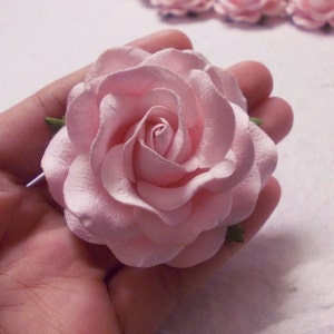 May include: A single, light pink paper rose with green leaves. The rose is made of paper and has a delicate, layered design.