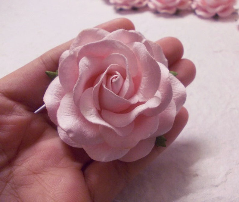May include: A single, light pink paper rose with green leaves. The rose is made of paper and has a delicate, layered design.