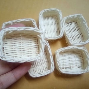 May include: Six white woven baskets of various sizes. The baskets are made of a woven paper material and have a natural, rustic look.