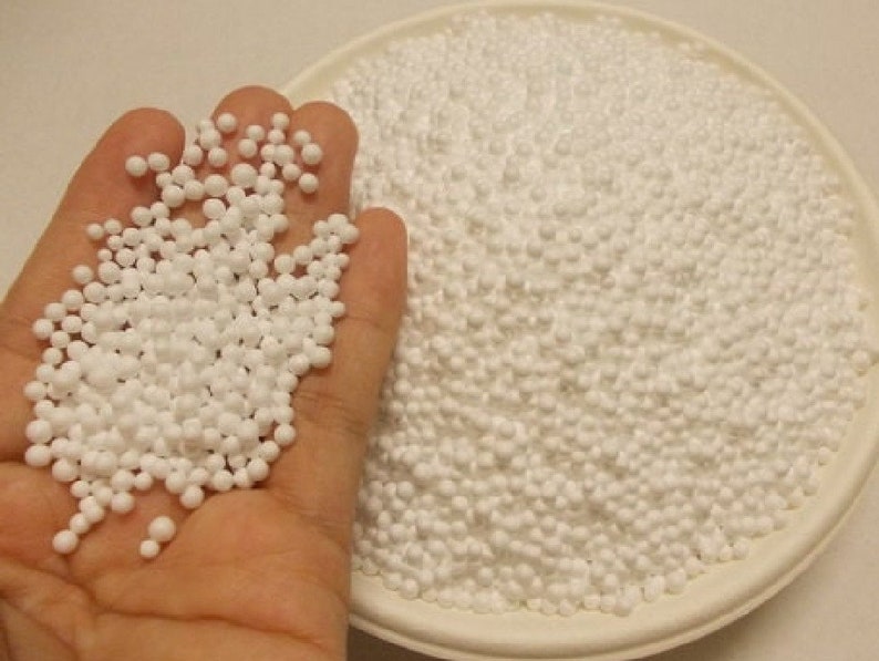 May include: A close-up of a white bowl filled with small, white polystyrene packing peanuts. A hand is holding a handful of the peanuts.
