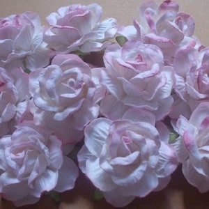 May include: A collection of 10 white paper roses with pink edges. The roses are arranged in a cluster and have a delicate, vintage look.