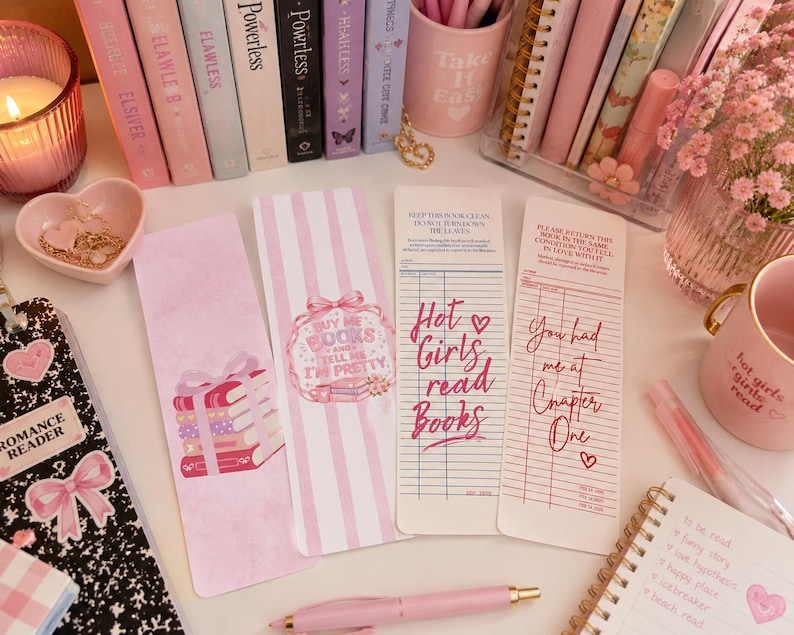 May include: Four rectangular paper bookmarks featuring pink and white designs. Two bookmarks display illustrations of stacked books and bows, while the other two resemble vintage library checkout cards with text reading Hot Girls read Books.