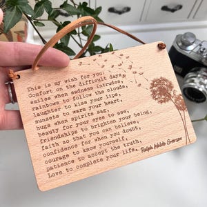 May include: A wooden plaque with a light brown background and a light brown string hanging from the top. The plaque has a quote engraved in a dark brown color. The quote is by Ralph Waldo Emerson. The quote reads: "This is my wish for you: Comfort on the difficult days, smiles when sadness intrudes, rainbows to follow the clouds, laughter to kiss your lips, sunsets to warm your heart, hugs when spirits sag, beauty for your eyes to see, friendships to brighten your being, faith so that you can believe, confidence for when you doubt, courage to know yourself, patience to accept the truth, Love to complete your life."