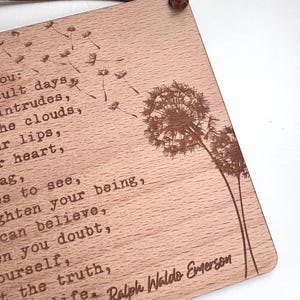 May include: Wooden sign with a quote by Ralph Waldo Emerson about trusting yourself and believing in the truth. The quote is engraved on a light brown wooden background with a dandelion design.