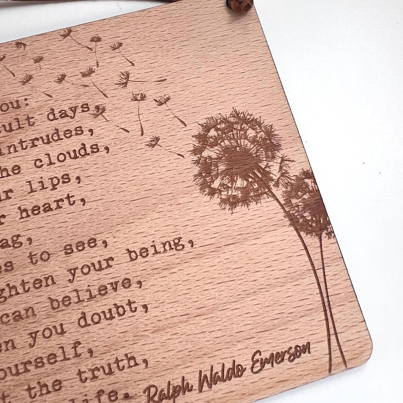 May include: Wooden sign with a quote by Ralph Waldo Emerson about trusting yourself and believing in the truth. The quote is engraved on a light brown wooden background with a dandelion design.