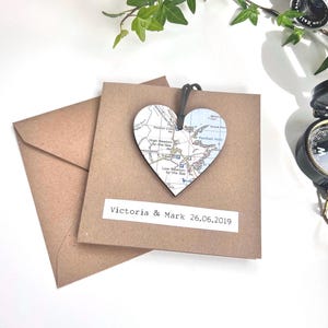 May include: A brown card with the text "Victoria & Mark 26.06.2019" and a wooden heart-shaped ornament with a map printed on it.
