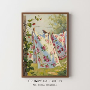 May include: A framed print of a vintage scene. Two floral patterned cloths hang on a clothesline, held by wooden clothespins. A small bird perches on the line. Strawberry vines and a grassy field are in the foreground. The text "GRUMPY GAL GOODS ALL THINGS PRINTABLE" is at the bottom.