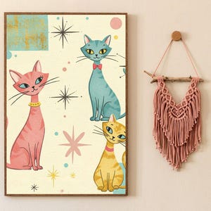 May include: A vintage-style print featuring three cats with different colored fur. The cats are set against a light yellow background with abstract shapes and stars. The print is framed in a brown wood frame.