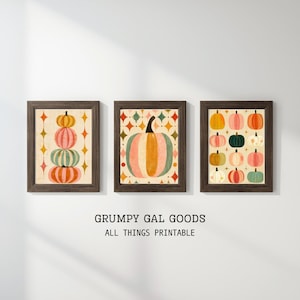 May include: Three framed wall art prints featuring pumpkin illustrations. The left print shows a vertical stack of four pumpkins with star shapes. The center print displays a large single pumpkin with a geometric background. The right print features a grid of twelve small pumpkins in various colors.