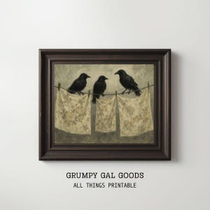May include: A framed print featuring three black crows perched on a clothesline above three floral patterned cloths. The artwork has a vintage aesthetic, with a dark brown frame and a neutral color palette. The text "GRUMPY GAL GOODS ALL THINGS PRINTABLE" is at the bottom.