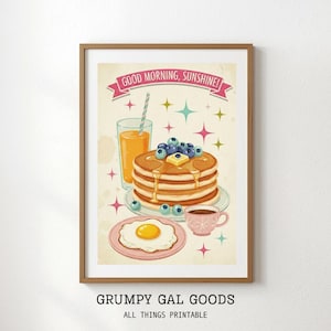 May include: A framed print featuring a retro-style illustration of a breakfast scene. It includes pancakes with blueberries, a glass of orange juice, a fried egg, and a cup of coffee. The text "GOOD MORNING, SUNSHINE!" is displayed on a banner.