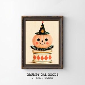 May include: A framed wall art print featuring a pale orange pumpkin character with a smiling face, wearing a dark green pointed hat with yellow stars. The pumpkin sits on a white cylindrical base decorated with a red diamond pattern and a green ruff.