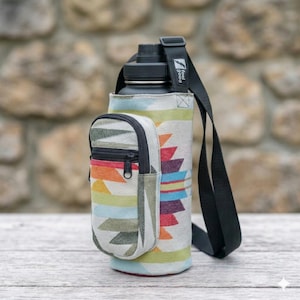 May include: A black water bottle in a colorful fabric carrier with a small zippered pouch. The carrier has a geometric pattern in shades of orange, green, blue, and purple. A black strap is attached to the carrier.